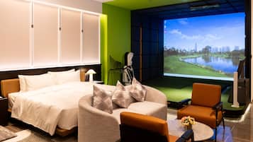 Een hotelkamer met een bed, een bank, een stoel, een klein tafeltje en een televisiescherm waarop een stadsgezicht te zien is.