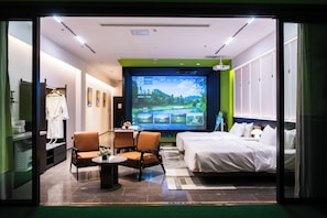 Habitació d'hotel amb un llit, un escriptori amb una cadira, un televisor que mostra un camp de golf, i un bany visible a través d'una porta oberta.