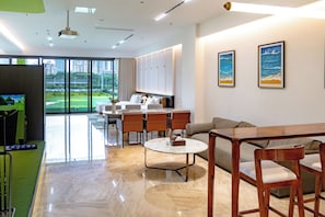 Habitación de hotel moderna con comedor, sofá, mesa de centro y vistas a un campo de golf.