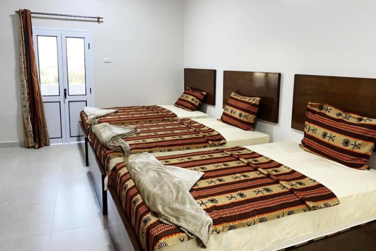 Una habitació d'hotel amb dos llits, una porta amb cortines i vista a l'exterior.