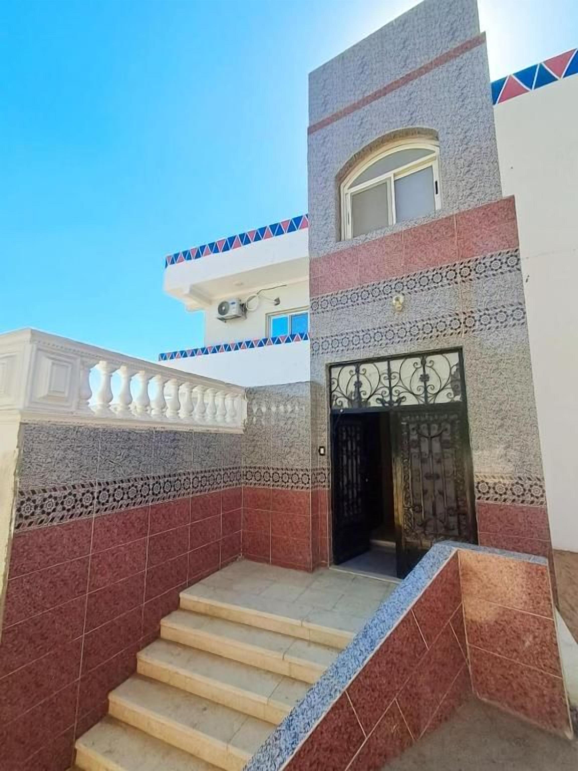 A building with a staircase leading to a gated entrance, patterned tiles, and a clear sky.
