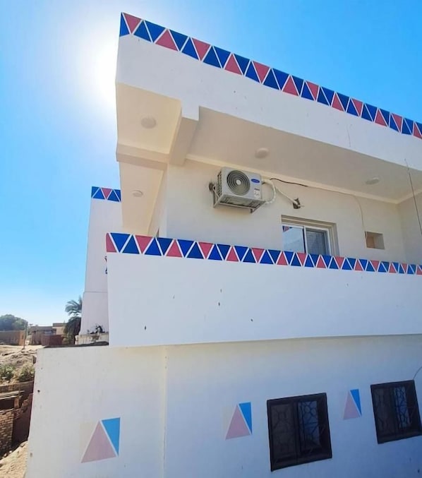 A building with a flat roof, a central air conditioning unit, and a window with a small balcony. - Nubian yellow desert (Aswan)