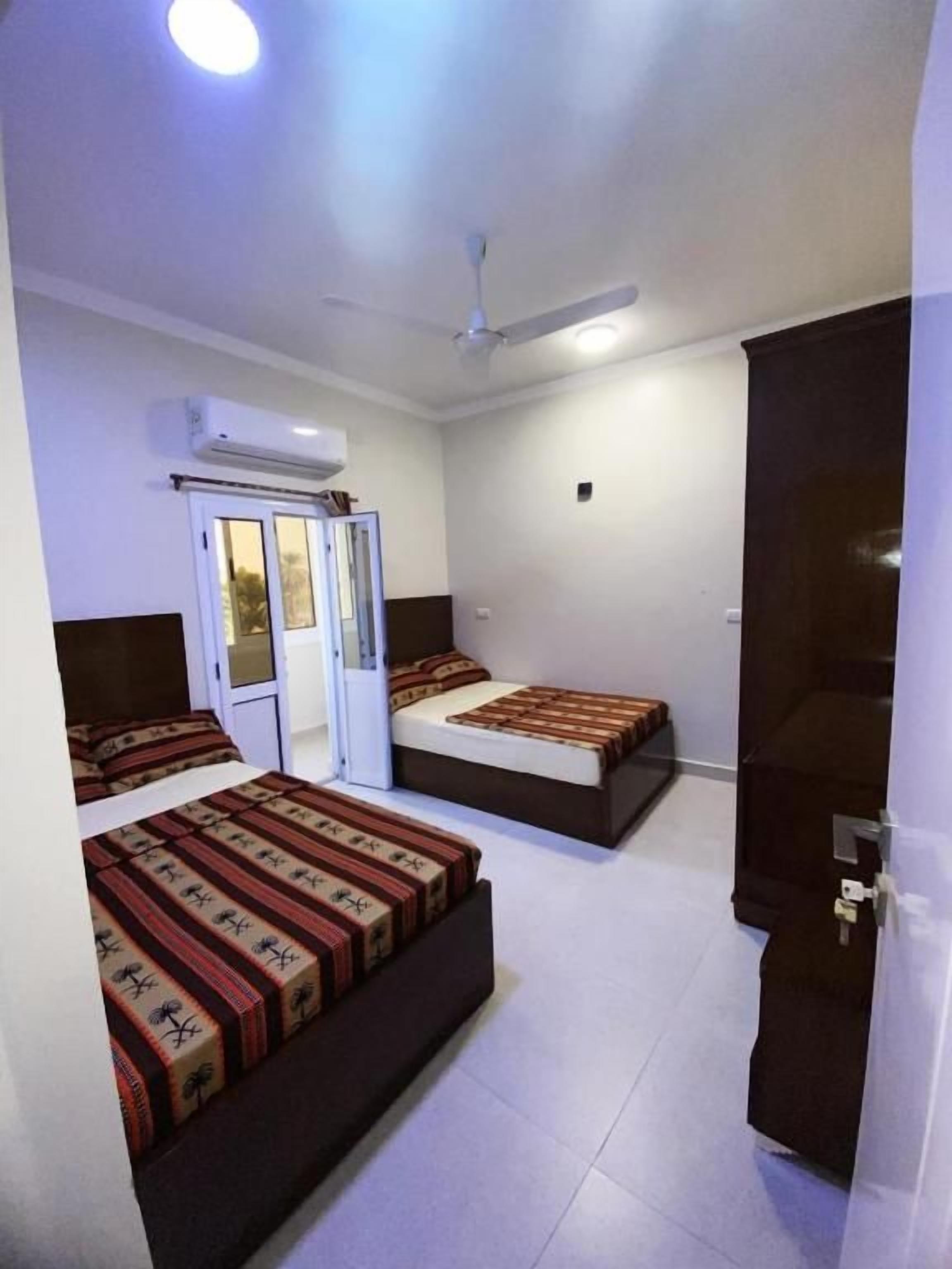 A room with two beds, a ceiling fan, an air conditioning unit, and a door.