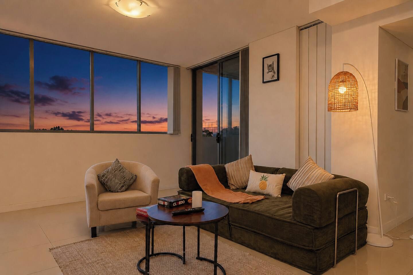 Ein Wohnzimmer mit Sofa, Sessel und Couchtisch. Ein großes Fenster bietet Blick auf den Himmel.
