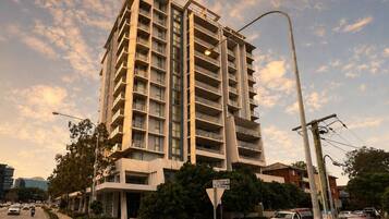 A multi-story building with balconies, located at an intersection with street signs.