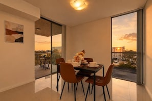A dining area with a table set for four, large windows offering a city view, and a modern interior design. - The Grove | 2BR | Free Parking | Sydney Airport-side Urban Escape | Close to CBD (Mascot)