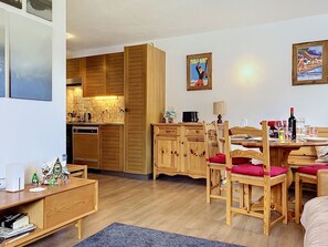 Ein gemütlicher, gut beleuchteter Raum mit Holzmöbeln, einem Essbereich mit Stühlen und Tisch sowie einer Küche mit Holzausbau und Geräten.