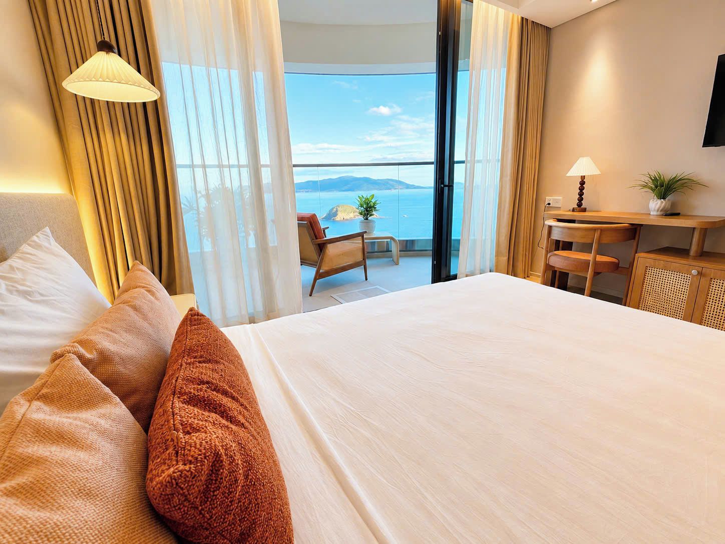 Quarto de hotel com uma cama grande, escrivaninha, cadeira e vista para o mar.