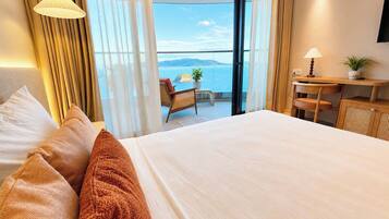 Quarto de hotel com uma cama grande, escrivaninha, cadeira e vista para o mar.