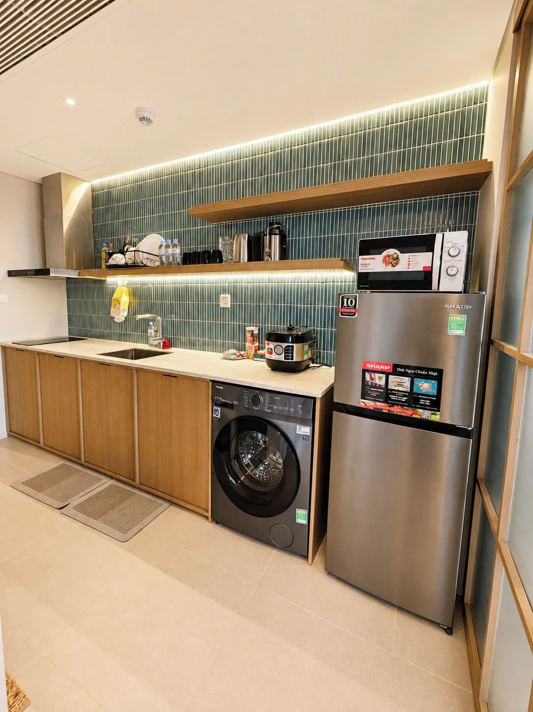 A modern kitchen with a built-in washing machine, a Sharp refrigerator, and a microwave.