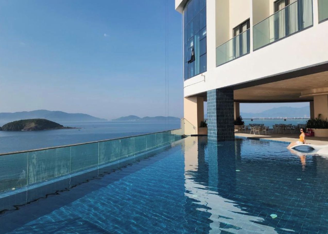 Un hotel moderno con piscina infinita en la azotea, con vistas a una masa de agua y tierra a lo lejos.