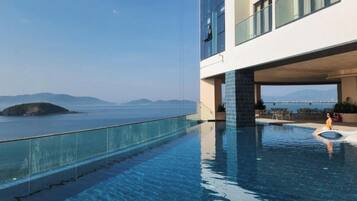 Un hotel moderno con piscina infinita en la azotea, con vistas a una masa de agua y tierra a lo lejos.