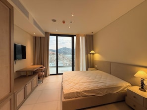 A hotel room with a bed, a TV, a desk, and a view of a mountainous landscape through the window. - The Paramount Nha Trang by San Village (Bac Nha Trang)