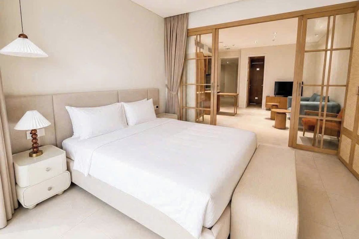 Quarto de hotel com uma cama grande, mesa de cabeceira com abajur, porta de vidro deslizante para uma varanda e uma televisão em um suporte.