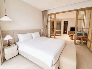 Quarto de hotel com uma cama grande, mesa de cabeceira com abajur, porta de vidro deslizante para uma varanda e uma televisão em um suporte.