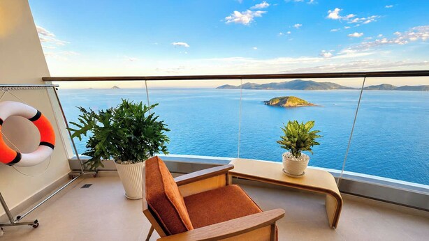 Varanda com vista para o mar, uma cadeira, duas plantas em vasos e um flutuador.