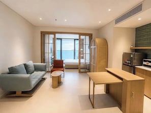 Uma sala de estar moderna com um sofá, uma poltrona, uma mesa pequena e uma área de cozinha com geladeira.