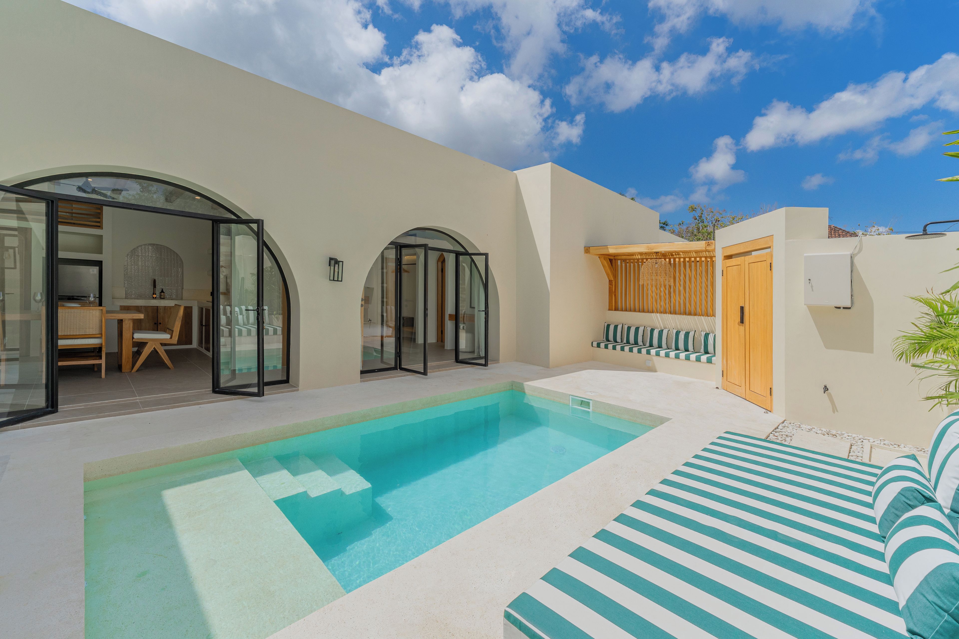 A modern outdoor pool area with a clear blue pool, a sun lounger, and a seating area with cushions.