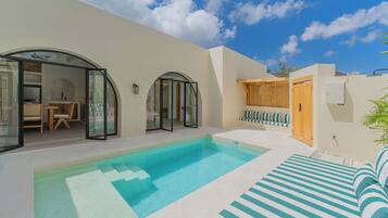 A modern outdoor pool area with a clear blue pool, a sun lounger, and a seating area with cushions.