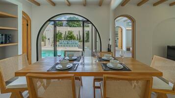 A dining area with a view of a pool and garden, wooden beams on the ceiling, and a glass door leading outside.