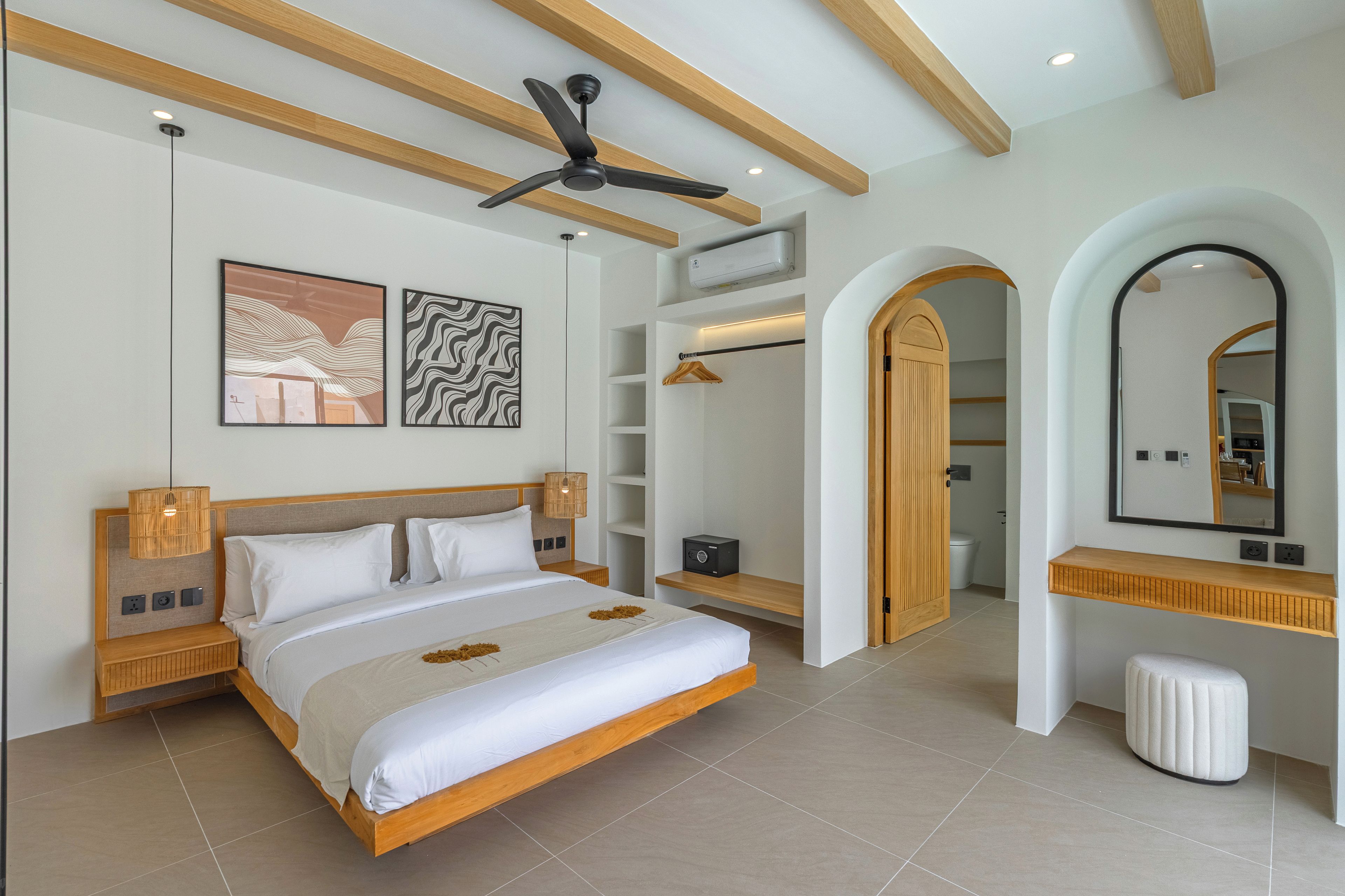 A modern bedroom with a large bed, a ceiling fan, a wardrobe, and a bathroom visible through an archway.