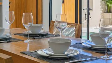 A dining table set with white bowls and wine glasses, a wooden chair, and a view through a glass door to the outside.