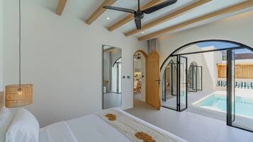 Un dormitorio con cama, ventilador de techo, un espejo grande y vista a una piscina.