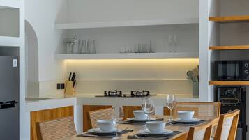 A modern kitchen with a dining area, featuring a central island with glassware, a built-in microwave, and a ceiling fan.