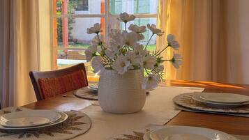 A dining table set with plates, a vase with white flowers, and a view through a window.