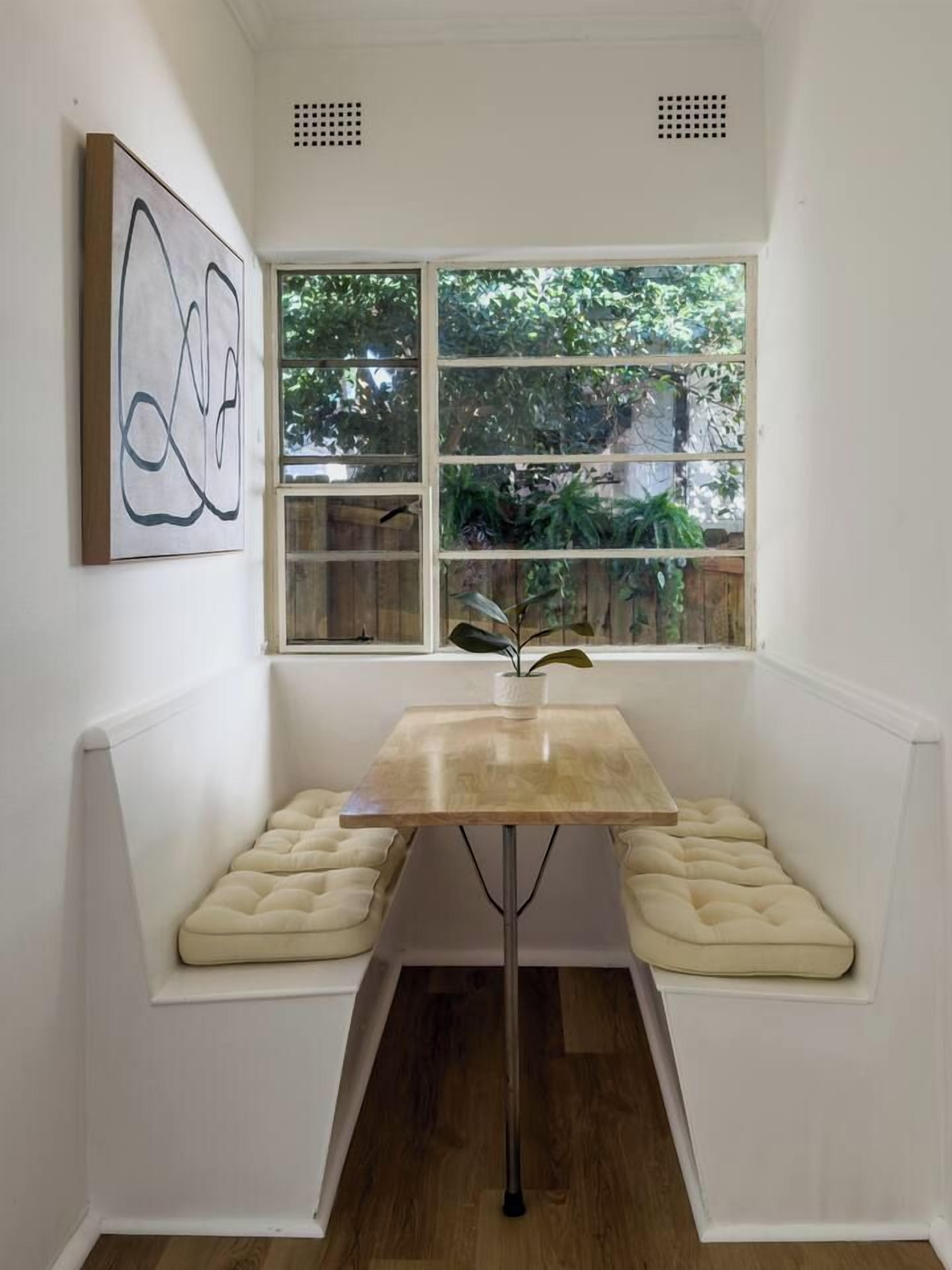A corner room with a window, a table, and a cushioned bench.