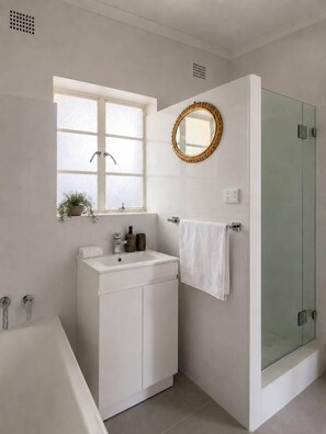 A modern bathroom with a bathtub, a sink, a glass shower enclosure, and a window with a plant. - Modern Mid-Century Epping Parkland (Epping)
