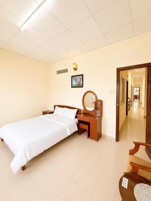 A hotel room with a bed, bedside table, mirror, and a door leading to a hallway. - KIM CHI HOTEL (Da Lat)