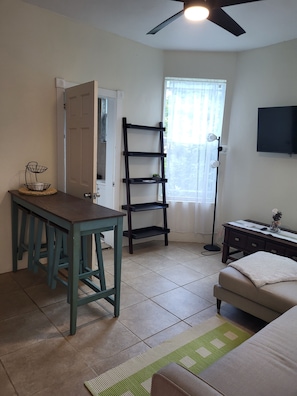 A room with a desk, a chair, a sofa, a ladder, a television, and a window with curtains. - Executive One-Bedroom Apartment Boasting Natural Light and Lush Scenery! (Charlotte Amalie)
