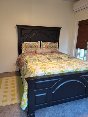 A bed with a patterned bedspread and pillows, a dark headboard, and a green and yellow rug. - Executive One-Bedroom Apartment Boasting Natural Light and Lush Scenery! (Charlotte Amalie)