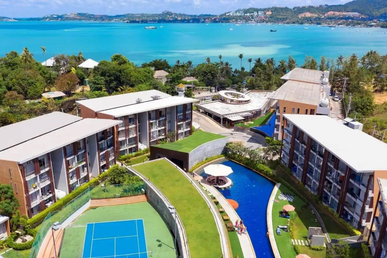 Un complexe hôtelier comprenant plusieurs bâtiments, une piscine et un court de tennis.