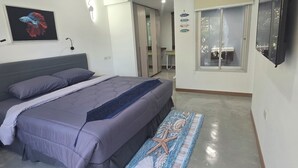 Une chambre à coucher avec un lit, un téléviseur fixé au mur, un tableau et un couloir menant à une salle de bain.