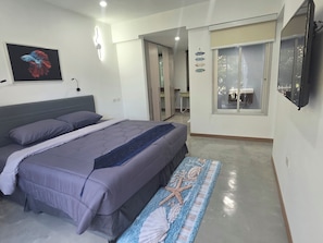 Quarto com cama, televisão na parede, um quadro e um corredor que dá para um banheiro.