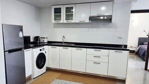 Une cuisine moderne dotée d’un réfrigérateur en acier inoxydable, d’un lave-linge encastré, de meubles blancs et d’un plan de travail noir.