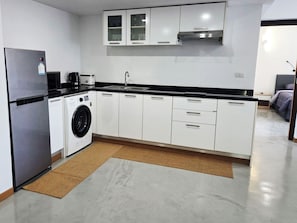 Cozinha moderna com frigorífico em aço inoxidável, máquina de lavar embutida, armários brancos e bancada preta.