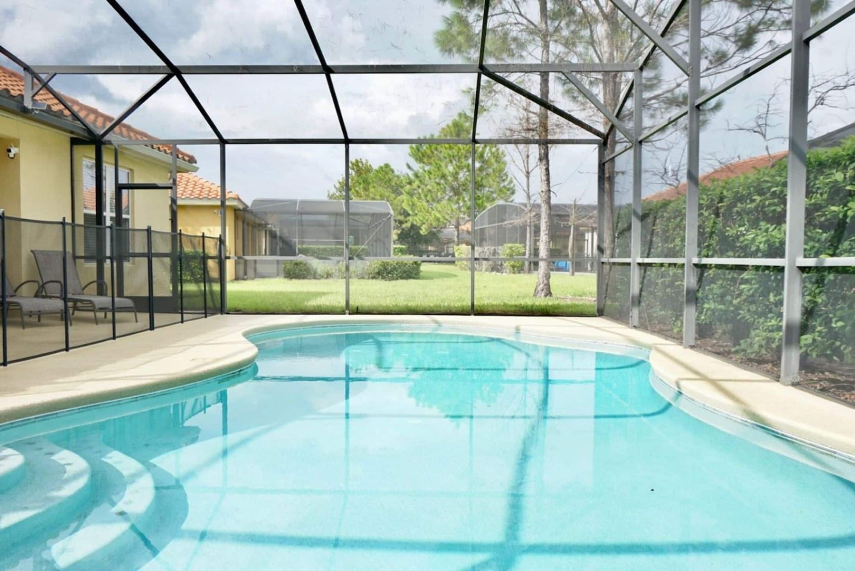 A swimming pool with a covered area, surrounded by a fence and trees.