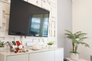 Une cuisine moderne avec un téléviseur à écran plat fixé au mur, un meuble blanc et une plante en pot.