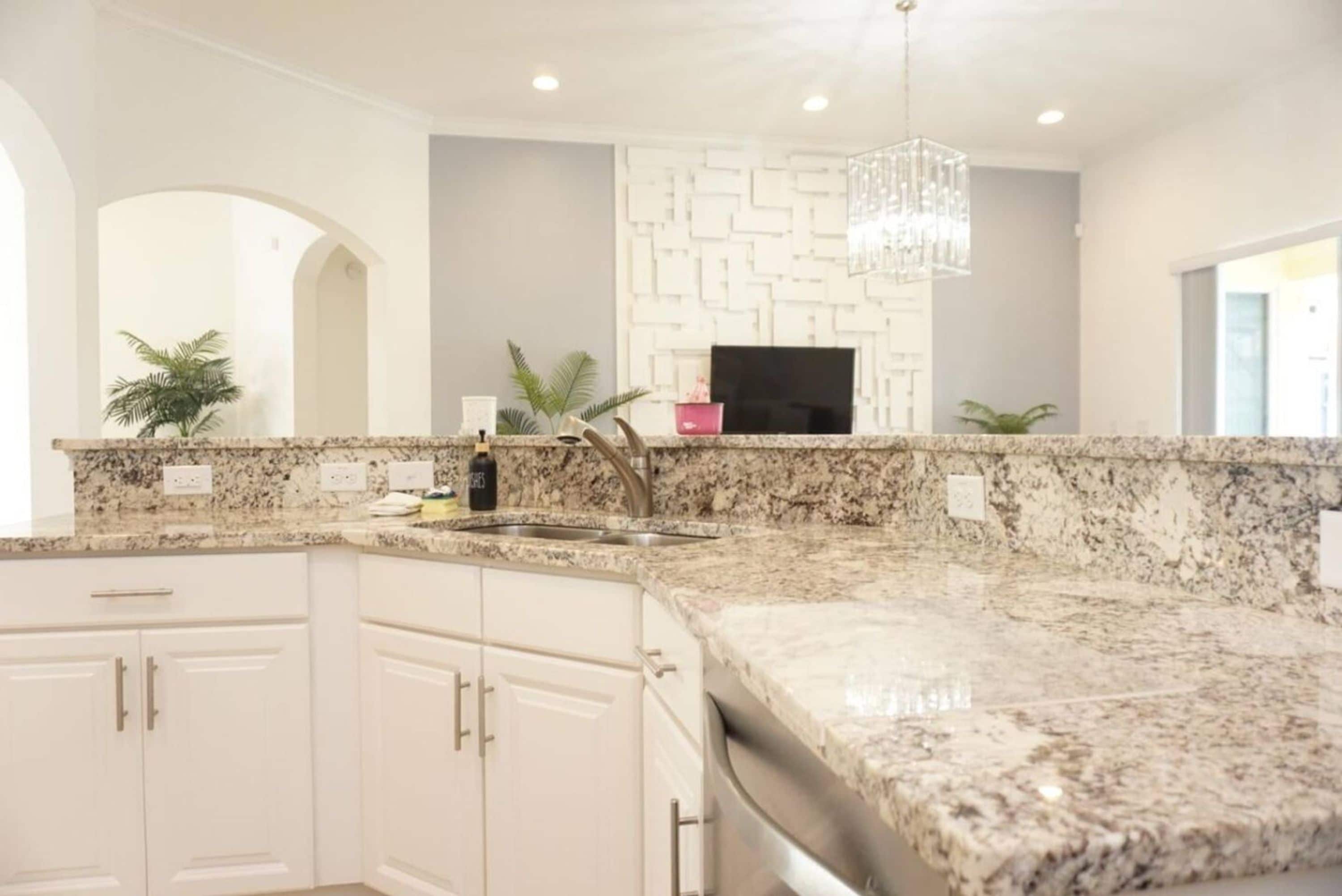 A kitchen with granite countertops, white cabinetry, a built-in oven, and a pendant light.