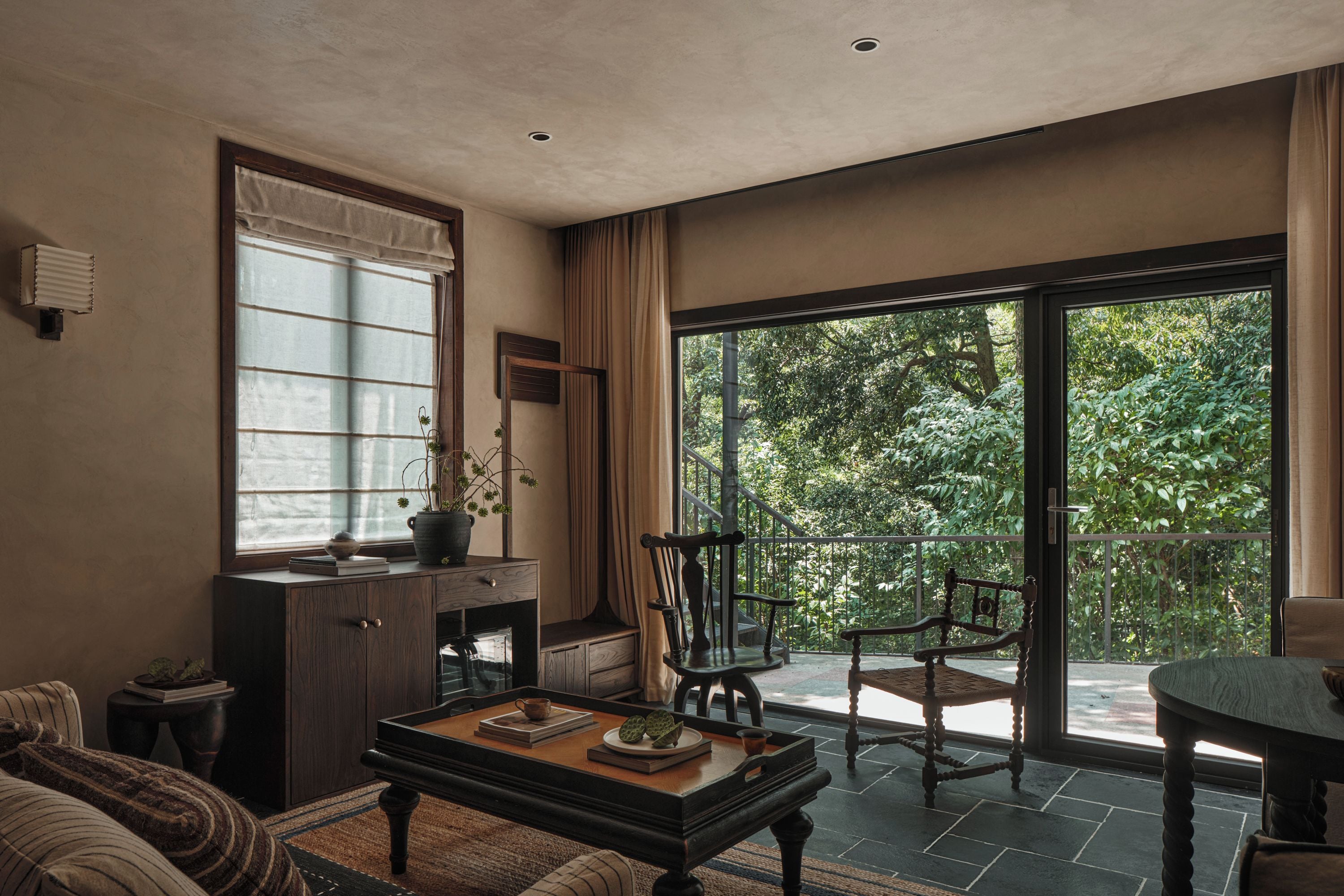 A spacious living room with a large window, a dining area with a table and chairs, and a view of a lush garden.