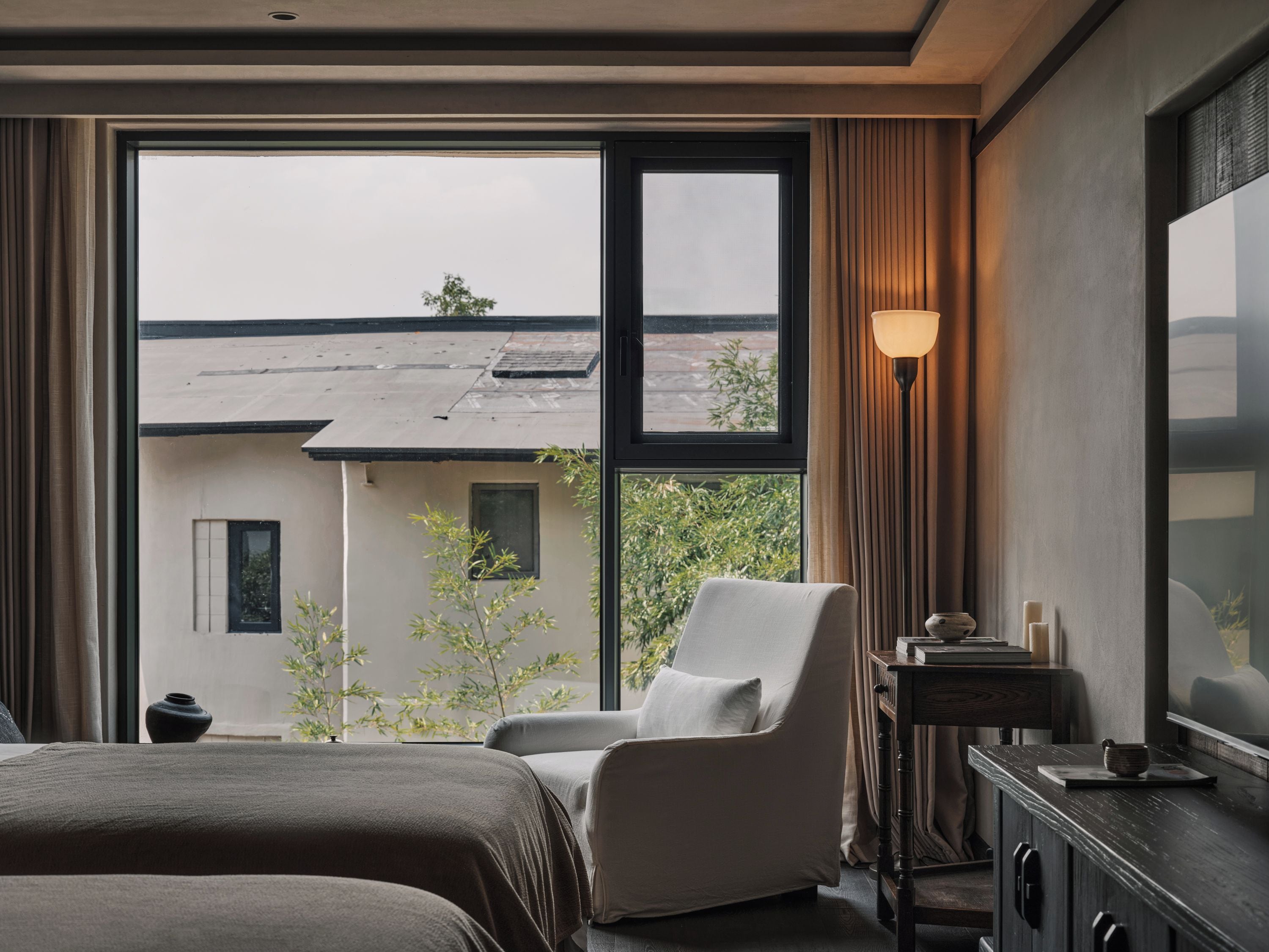 A hotel room with a large window, a bed, a chair, a bedside table, and a TV.