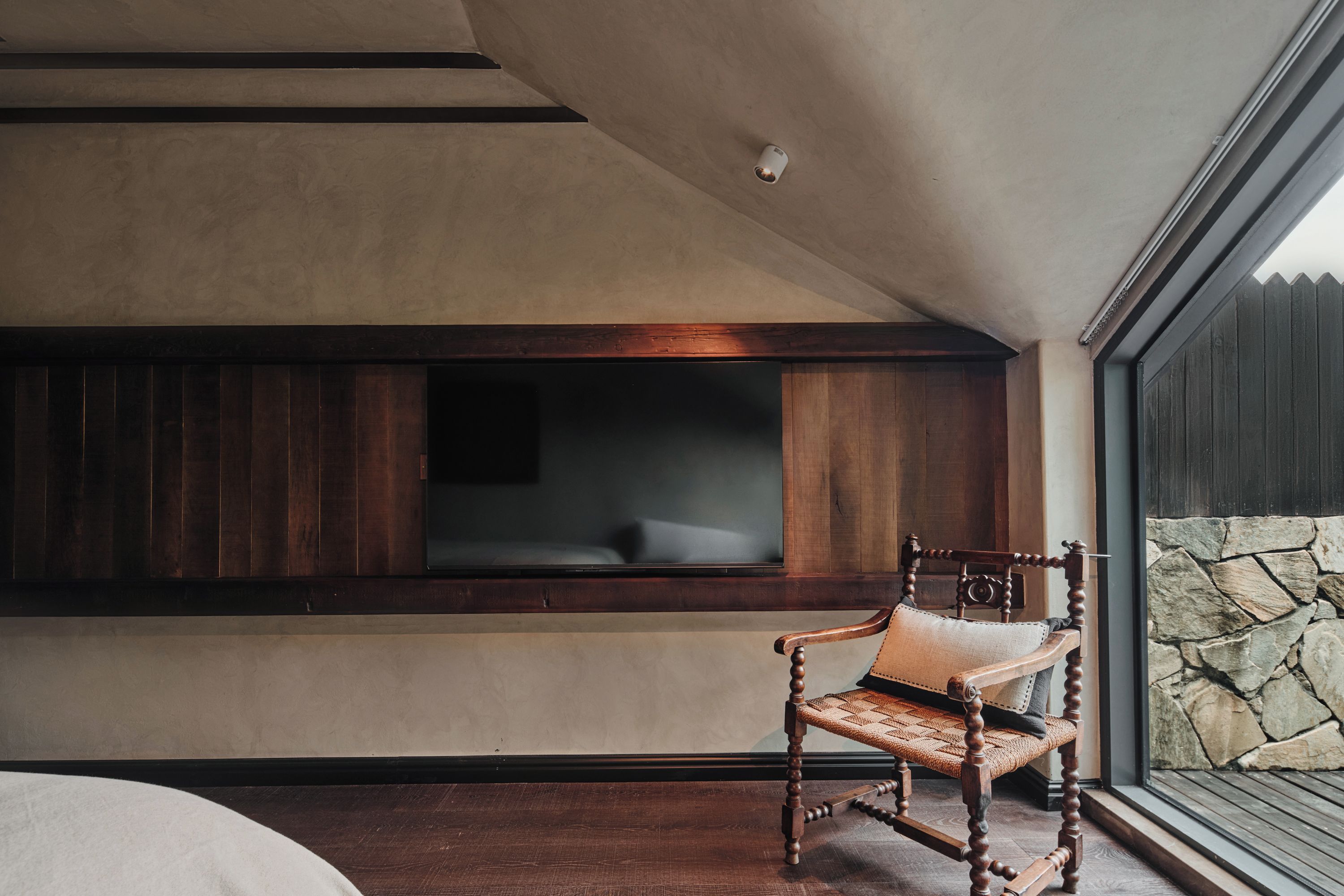 A room with a large window, a wooden chair, and a stone wall.