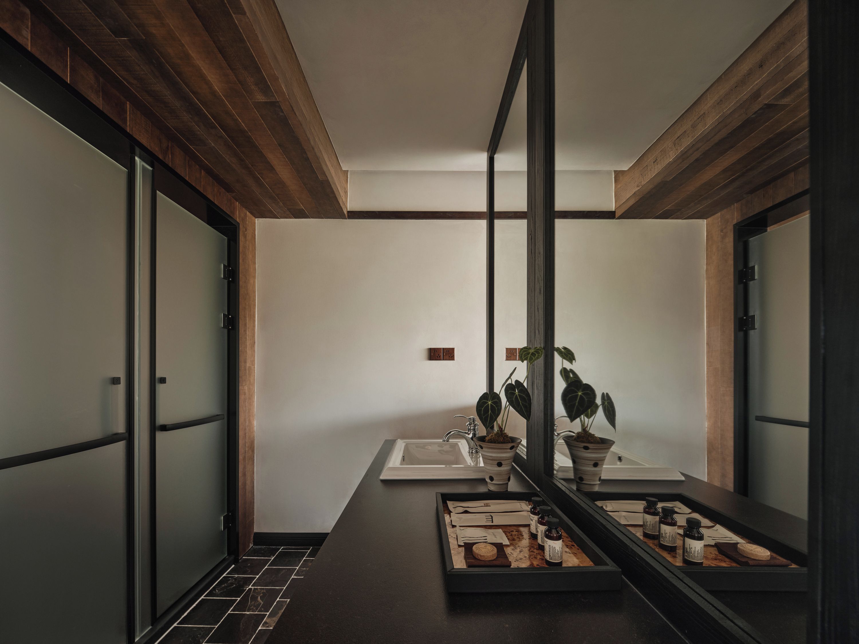 A modern bathroom with a wooden ceiling, a large mirror, and a tray with toiletries.