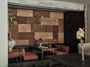 A modern interior with a wooden wall panel, a dining table, seating, and a hanging light fixture.