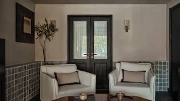 A room with two white armchairs, a wooden coffee table with books and a decorative item, a door with a window, and a wall-mounted picture.