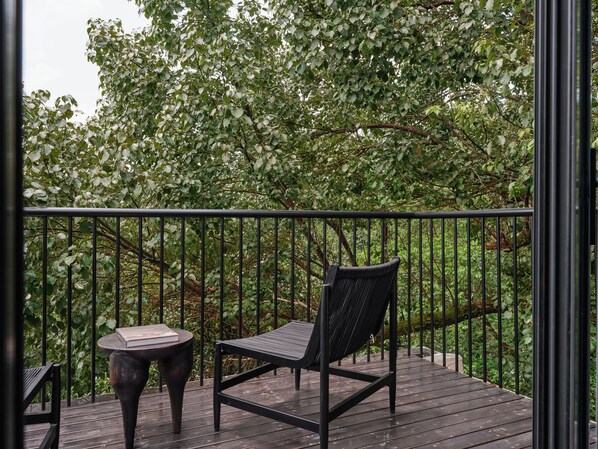 A wooden deck with a metal railing, a black chair, and a small round table.