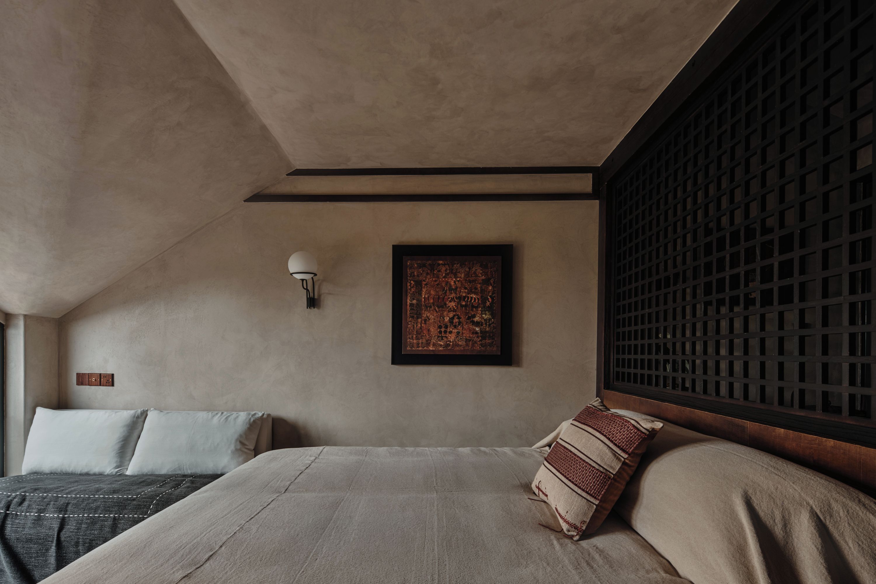 A bedroom with a bed, pillows, a wall-mounted light, and a framed artwork.